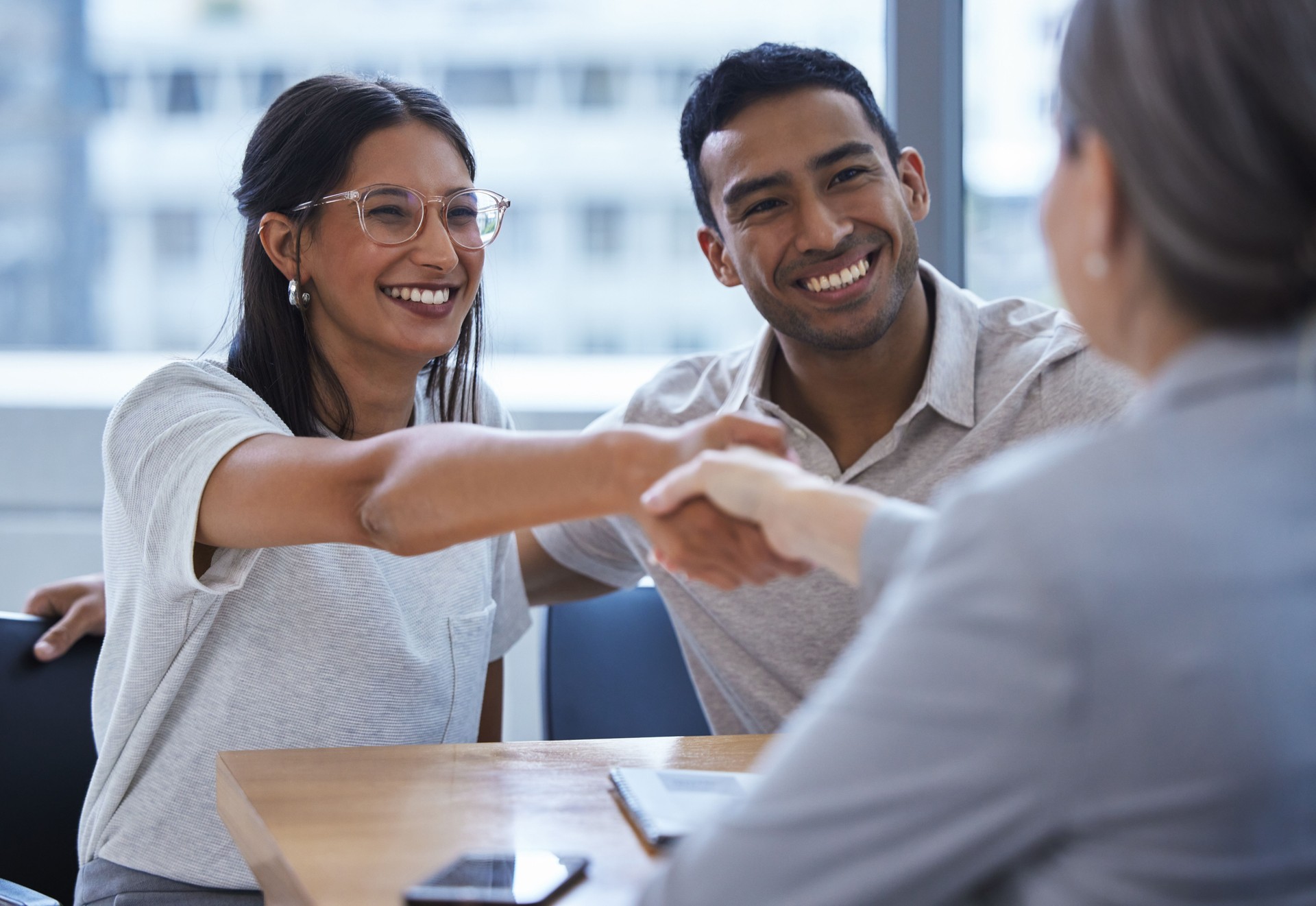 Foto de una pareja joven compartiendo un apretón de manos con un consultor que están reuniendo para discutir el papeleo de una oficina