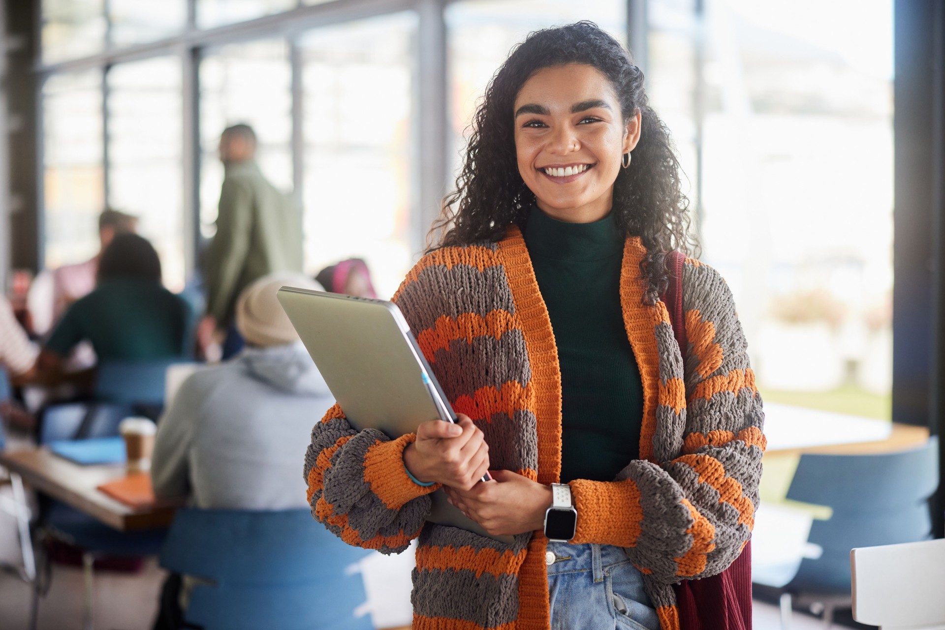 Estudiante joven sonriente de pie con una computadora portátil en una cafetería universitaria